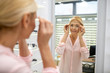 © zinkevych - Long-haired woman looking in the mirror to choose glasses frame