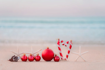 Christmas ball and starfish on yellow sand and sea background. New Yeaar or Xmas holiday vacation in exotic countries or tropics concept: christmas decorations on the beach. Copy space for text