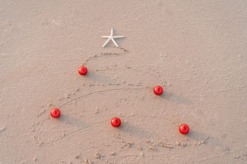 Xmas tree picture draft on sand  Christmas ball and starfish. New Yaar holiday vacation in exotic countries or tropics concept: christmas decorations on the beach. Copy space text