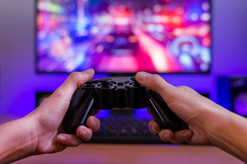 Fototapete - Joypad in hands. Gaming concept. Computer display with racing game and rgb light in background.