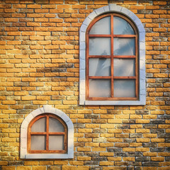 Wasting away orange vintage brick walls. Background of brick wall is yellow with two windows. Texture of the old stained brickwork and wooden windows, close-up.