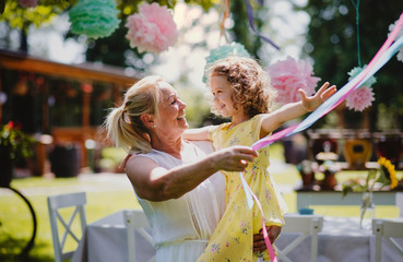 Grandmother holding small girll outdoors on garden party in summer.