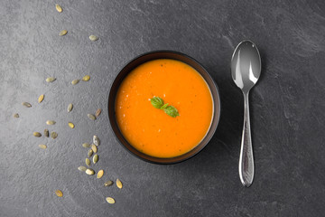 Wall Mural - food, new nordic cuisine, culinary and cooking concept - close up of vegetable cream soup in bowl, pumpkin seeds and spoon on slate stone background