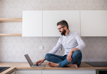 Wall Mural - A mature man with laptop sitting in kitchen in unfurnished new house.