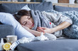 © Monstar Studio - Sick exhausted girl in scarf is lying in bed wrapped in blanket. Young woman with fever and headache is measuring temperature with thermometer, treated at home. Winter cold and flu concept.
