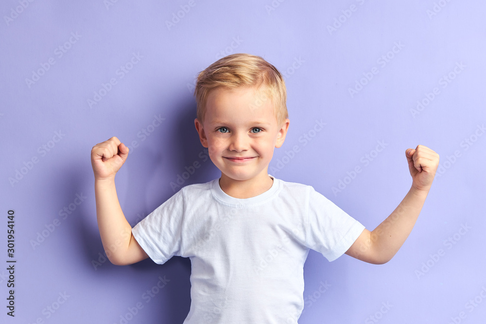 Winner kid isolated over purple background, show how powerful he is. Isolated over purple background - obrazy, fototapety, plakaty 