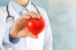 © Atlas - Doctor holds heart against blue background, close up