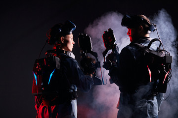 Wall Mural - Man and woman stand opposite each other, team in virtual reality game. Isolated over black smoky background