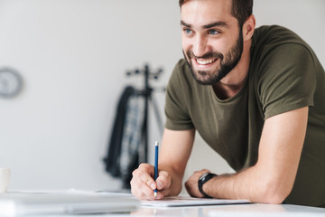 Poster - Image of young smiling caucasian man reading documents and making notes