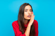 Young woman with red sweater over isolated blue background whispering something