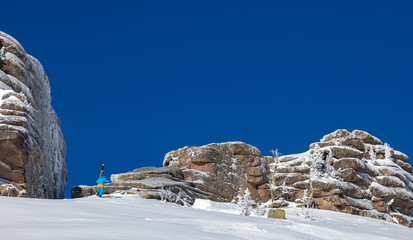 professional Freerider climbs with skis on his shoulder high in the mountains, against the background of beautiful snow-capped rocks and bright blue sky. Out-of-piste skiing. Epic free ride scene