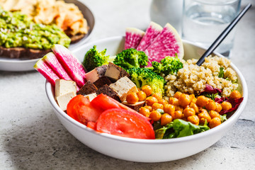 Buddha bowl with quinoa, fried chickpeas, smoked tofu and vegetables in white plate. Healthy vegan food concept.