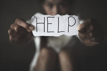 women sitting alone with depressed expression and showing a paper with a help text. Ideas to stop violence against women, sexual harassment and rape, human trafficking