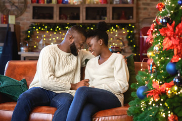 Wall Mural - Romantic afro couple sitting on sofa near Christmas tree