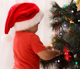 Wall Mural - Cute baby in Santa hat playing with decorations on Xmas tree