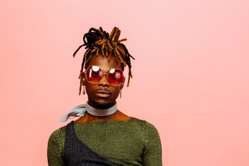 Wall Mural - Portrait of a serious young man in green with dreadlocks and red sunglasses, isolated on pink