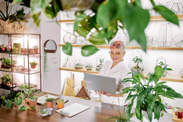 Wall Mural - Senior business lady using laptop, view from above. Business connected to flora. Plants, greenery concept