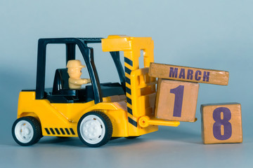 march 18th. Day 18 of month, Construction or warehouse calendar. Yellow toy forklift load wood cubes with date. Work planning and time management. spring month, day of the year concept