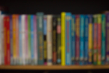 Blurred background with colorful books: university or college textbooks and fiction. Bookshelf at home or library. Concept for knowledge or education as well as imagination