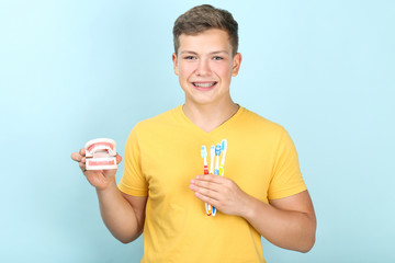 Wall Mural - Young man with toothbrushes and teeth model on blue background