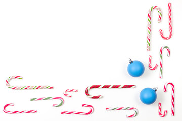 Candy canes and two blue Xmas decoaration bauble balls frame on white background. Top view