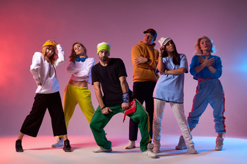 Active cheerful dancers posing over pink background after concert, having photo session in dance studio, dressed in sportive clothes