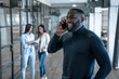 © Roman - Quick business talk. Handsome young african american smiling man talking on the phone and gesturing while his colleagues standing in the background