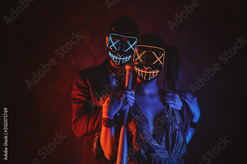 Cuadros en Lienzo Man and woman in masks are posing for photographer with baseball bat in red and blue lights