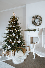 Wall Mural - Christmas tree with boxes of gifts and a chair stands near the fireplace and other holiday decorations in white room