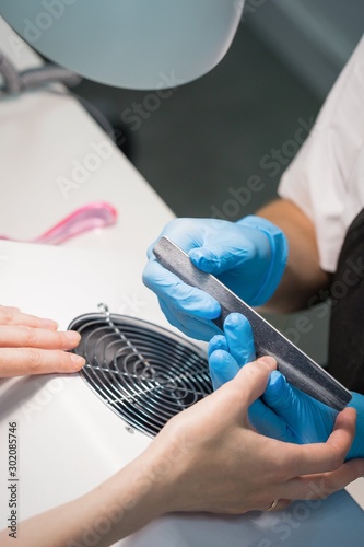 Cuadros en Lienzo Manicurist in blue hygienic gloves do manicure of nails in beauty salon