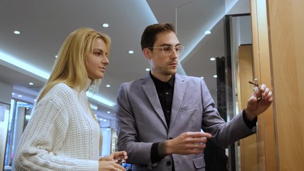 Poster - Attractive blond woman is asking for store consultant to try pair of glasses from showcase. She is trying on them.