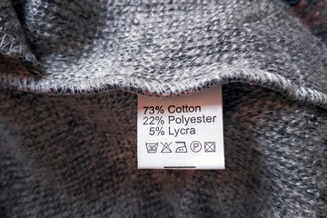 Wrong side of a gray dress made of wool, the composition is specified: cotton, polyester and lycra. Fabric composition clothes label on gray texture background.