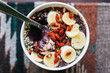 Silver spoon scooping out bite of acai bowl topped with dried goji berries, seeds, and sliced banana