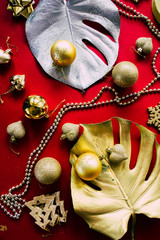 Exotic christmas celebration, two giant monstera leaves painted golden and silver with goldne christmas dcoration on a red background, top view, christmas luxury concept.