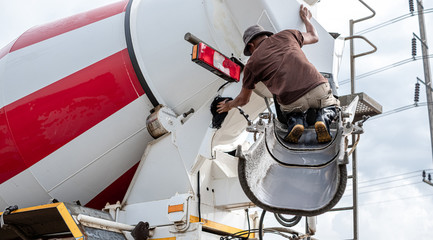 truck driver washing the cement mixer truck after finish pouring cement. man standing on the cement 