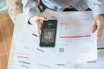close up hand holding smart phone to scan qr code from invoice on papers for the bills. finance tech