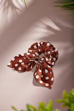 Object Photo Of A With  Brown White Polka Dot Scrunchie, Decorating With Big Bow. The Scrunchie Is Lying On A Beige Background. There Are Leaves In Corners Of A Photo. 