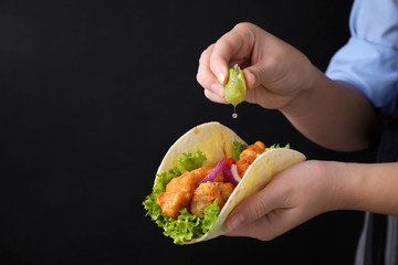 Woman squeezing lime on fish taco against dark background, closeup