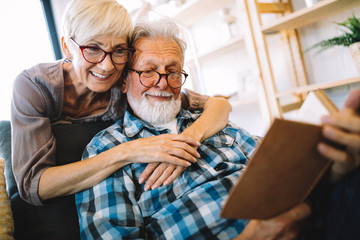 Beautiful old couple is reading a book and smiling at home