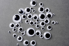 Many Different Sizes Of Googly Eyes On Grey Background.