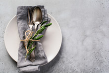 Rustic Vintage Set Of Cutlery. Plate With Grey Linen Napkin, Fork And Spoon, Olive Tree Branch Over Rustic Concrete Gray Old Background. Fall Holiday Table Decoration Setting. Top View, Copy Space.