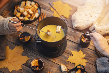 Top view friends cooking Swiss fondue assorted cheeses dinner on fire, hands holding mulled wine background wood board