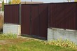 © butus - brown closed gate and metal fence on a gray concrete foundation in green grass