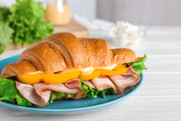 Tasty croissant sandwich with ham on white wooden table, closeup