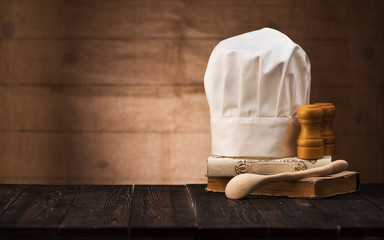 Chef's hat, vintage cookbooks and wooden spoon on the kitchen table with space for text.   cooking concept