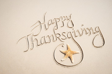 Happy Thanksgiving message handwritten on smooth sand beach with decorative starfish