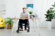© LIGHTFIELD STUDIOS - Smiling freelancer in wheelchair using laptop at desk in living room
