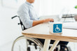 © LIGHTFIELD STUDIOS - Selective focus of cube with disabled sign and man in wheelchair sitting at table
