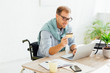 © LIGHTFIELD STUDIOS - Smiling man in wheelchair holding credit card and using laptop at table