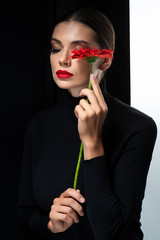 beautiful woman with red lips and closed eyes holding red gerbera isolated on white and black